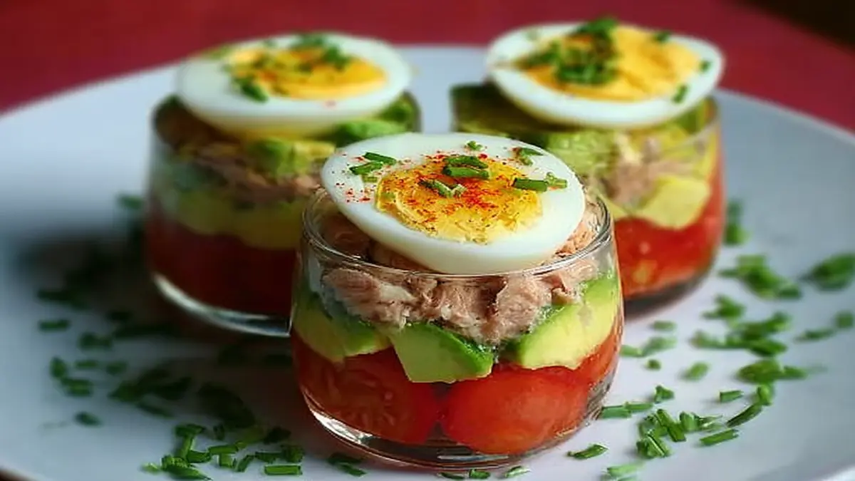 Verrine de thon à l'avocat et œuf dur, servie en couches colorées sur assiette blanche